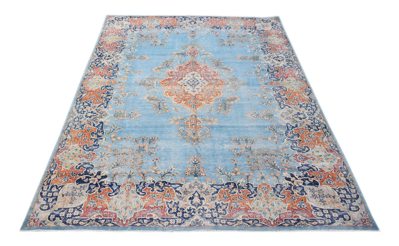 A vintage Persian Kerman rug featuring a central medallion and floral motifs in blue and orange.