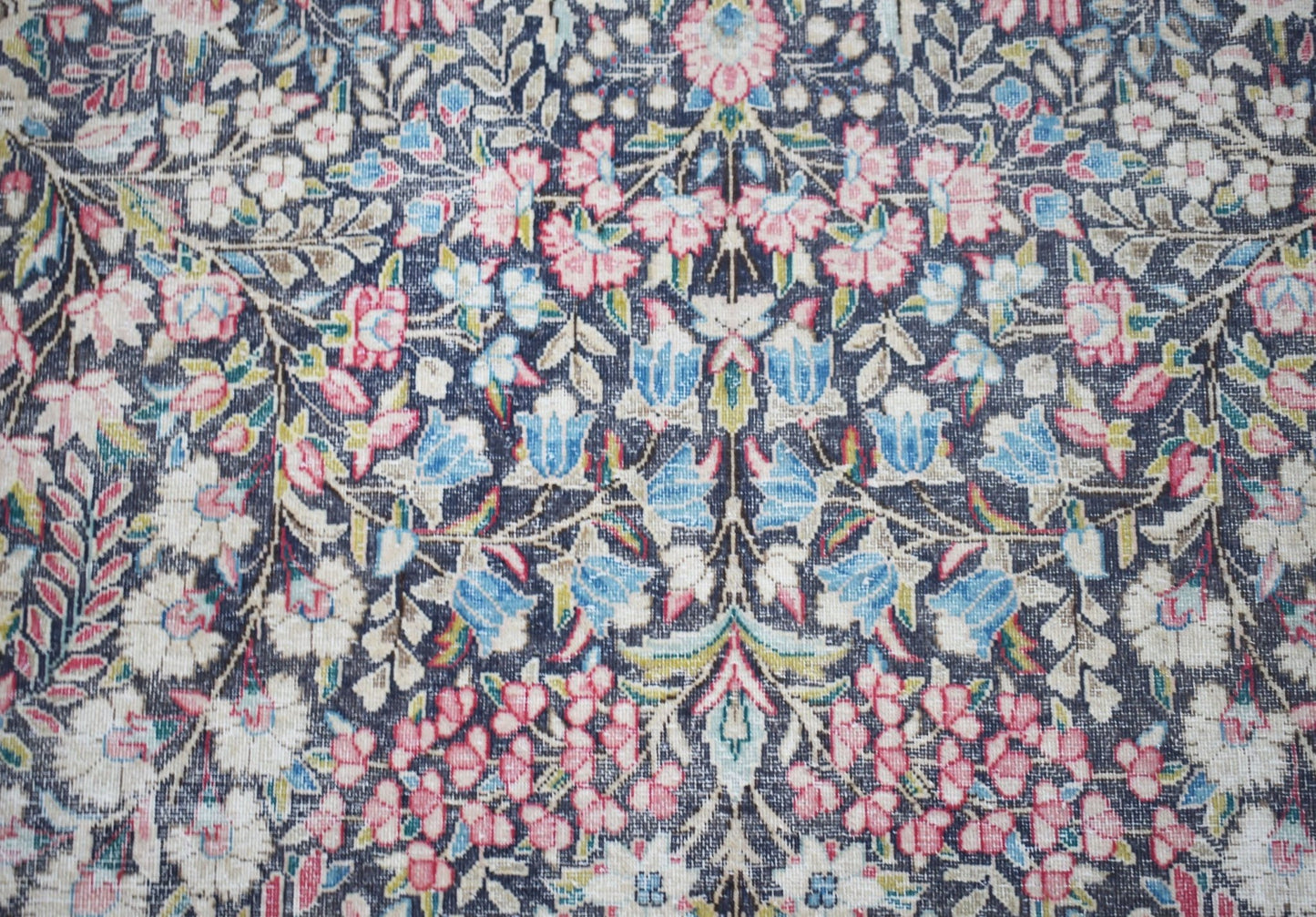 Vintage Persian Kerman rug with a floral pattern in pink, blue, and white on a dark background.