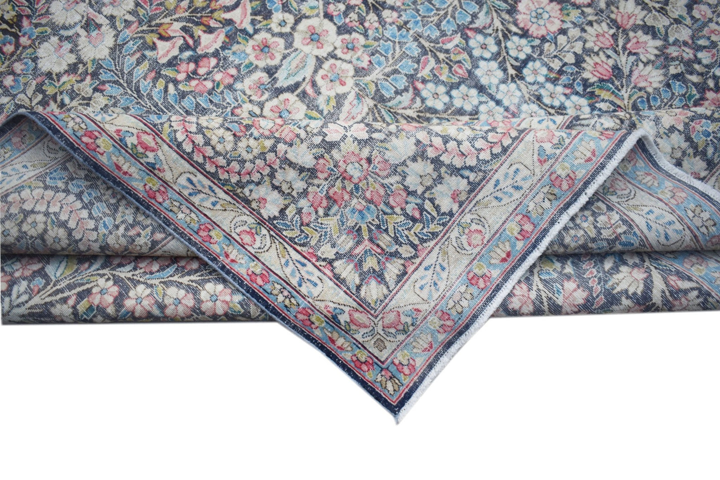 A vintage Persian Kerman rug featuring an intricate floral pattern in soft pink and blue tones.