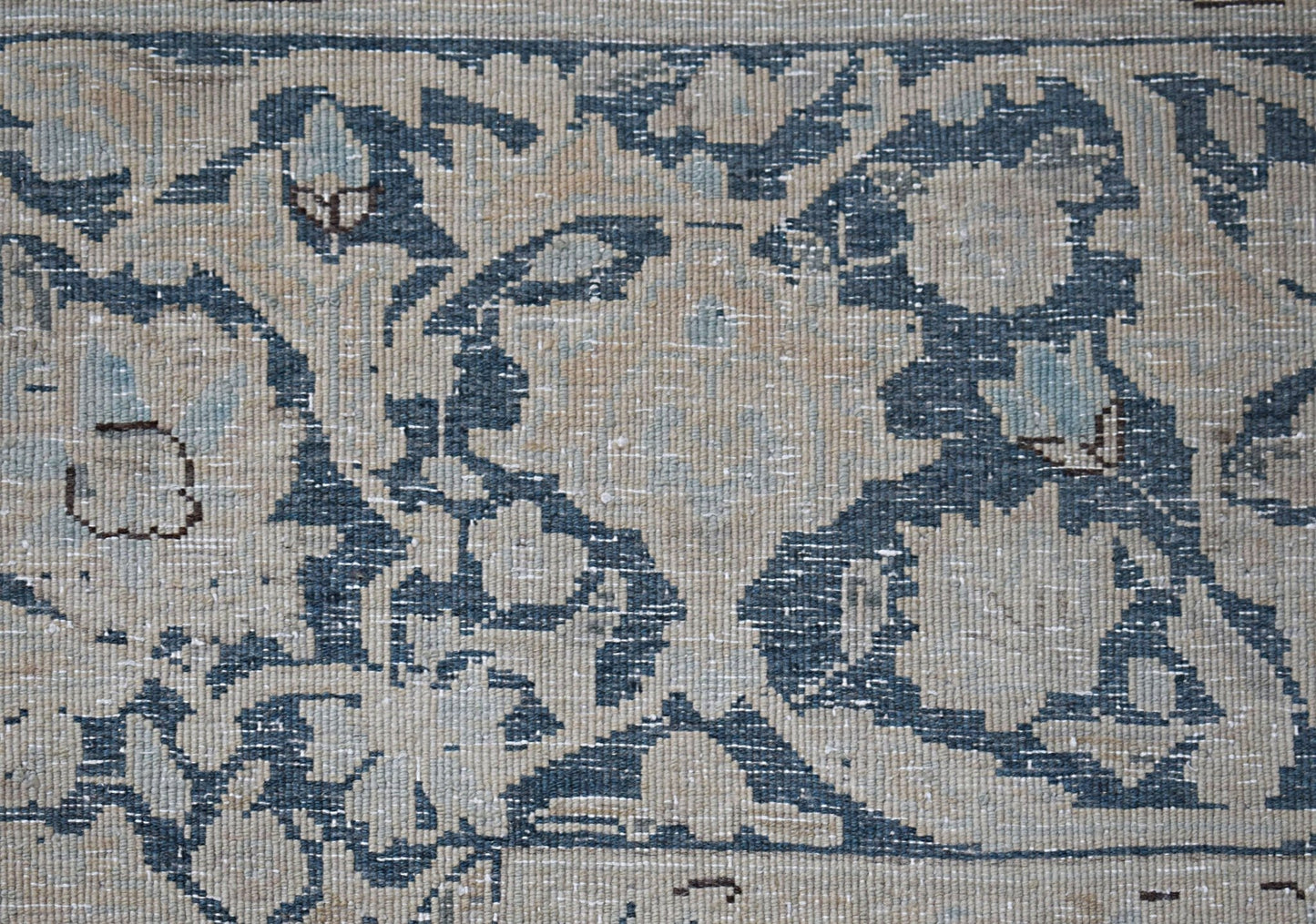 A close-up of a vintage Persian Kerman rug featuring intricate blue and beige floral patterns.