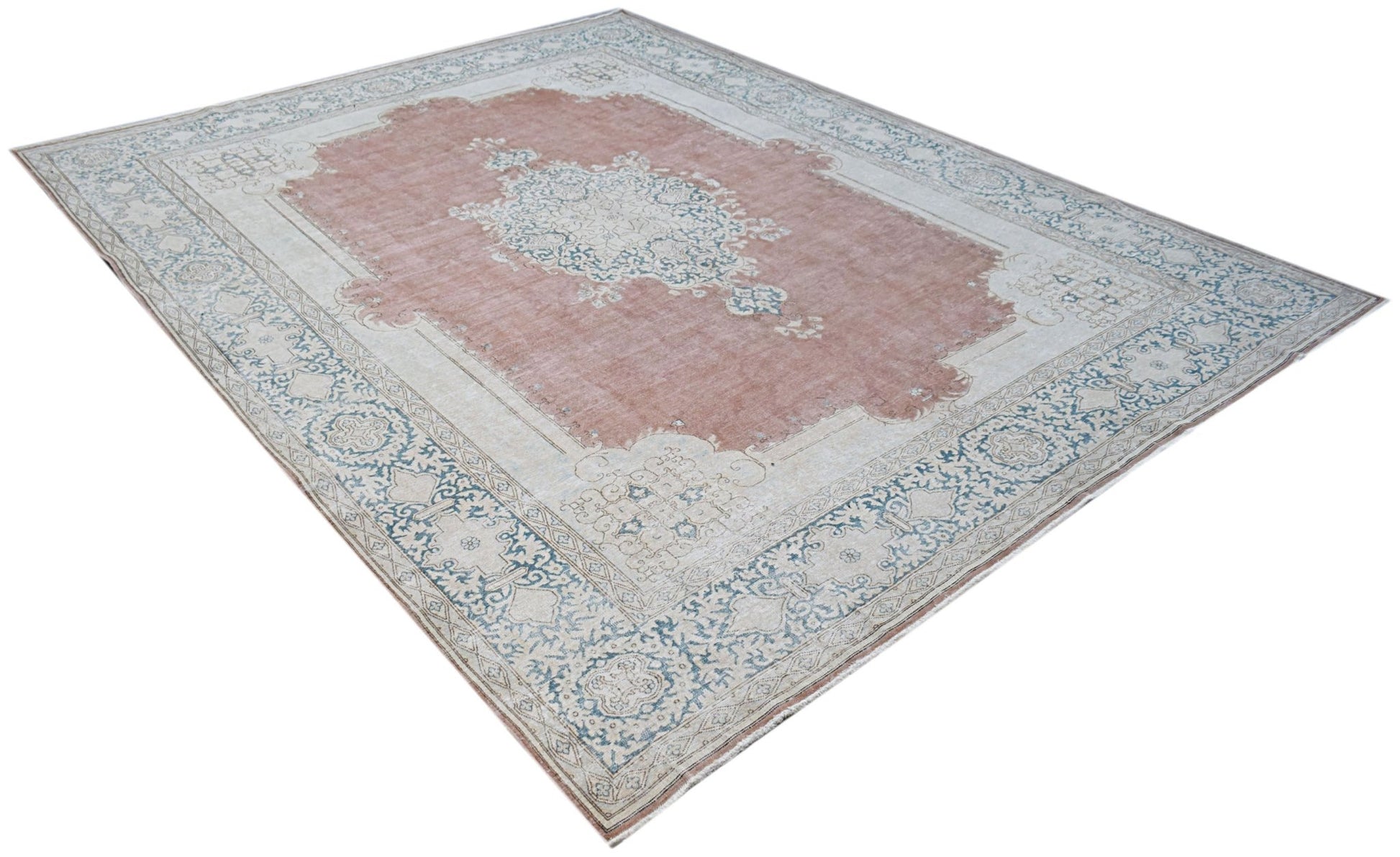 A vintage Persian Kerman rug featuring a central medallion on a dusty pink field with floral borders.