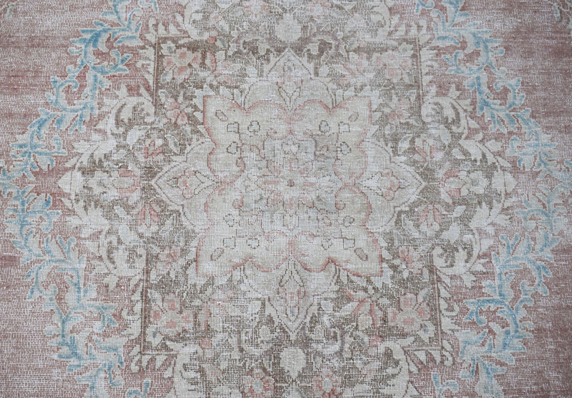 A vintage Persian Kerman rug featuring a central floral medallion in muted pink, blue, and beige.