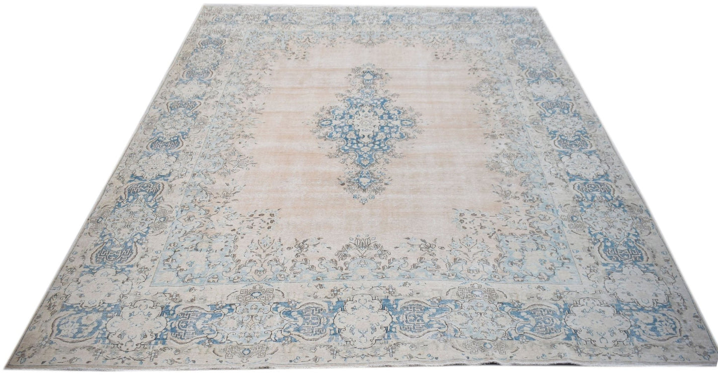 A vintage Persian Kerman rug featuring a central blue medallion on a soft beige floral field.