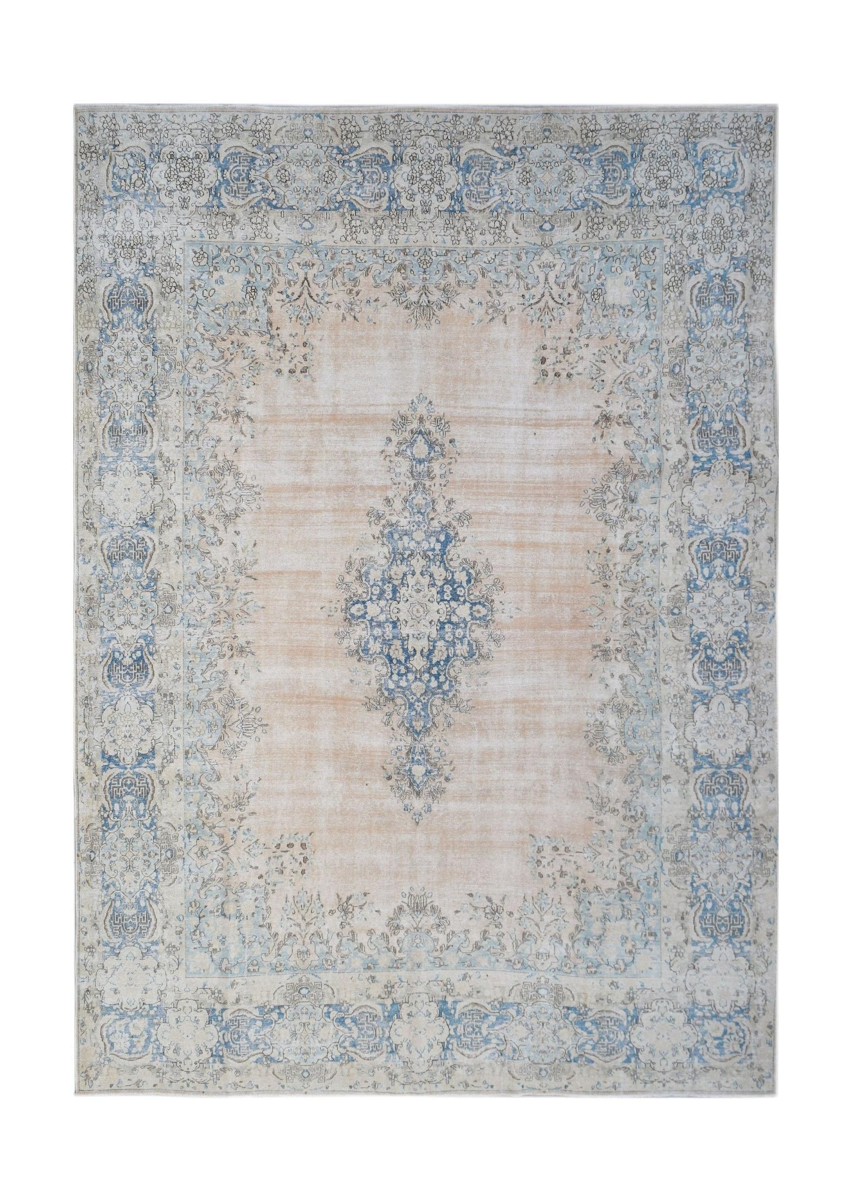 A vintage Persian Kerman rug featuring a central blue medallion on a soft peach field.
