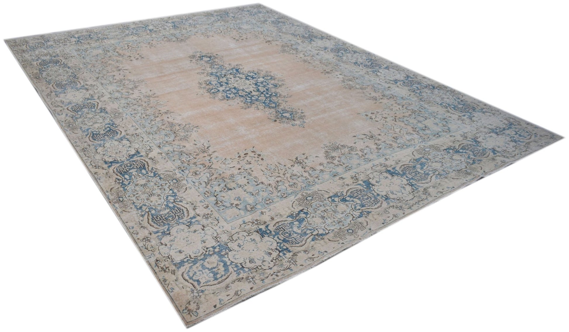 A vintage Persian Kerman rug featuring a central blue medallion on a soft peach background.
