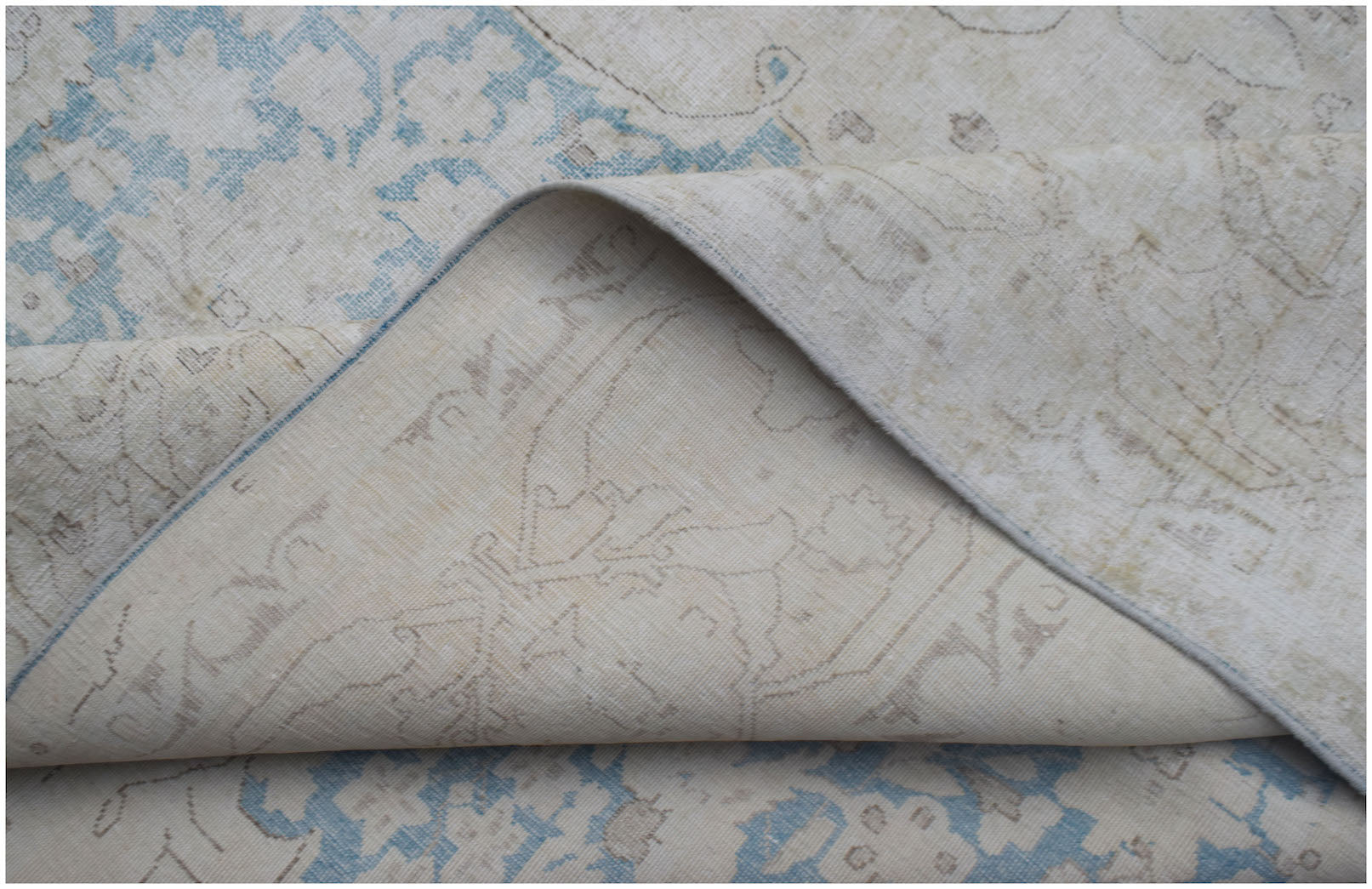 A vintage Persian Kerman rug with a light blue and beige floral pattern, shown folded.