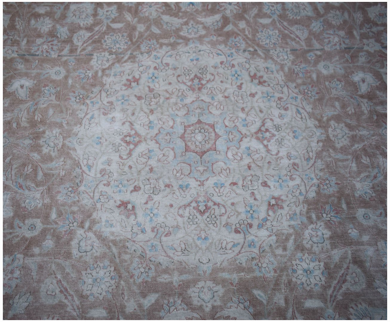 A vintage Persian Kerman rug featuring a central floral medallion in soft pink and blue tones.