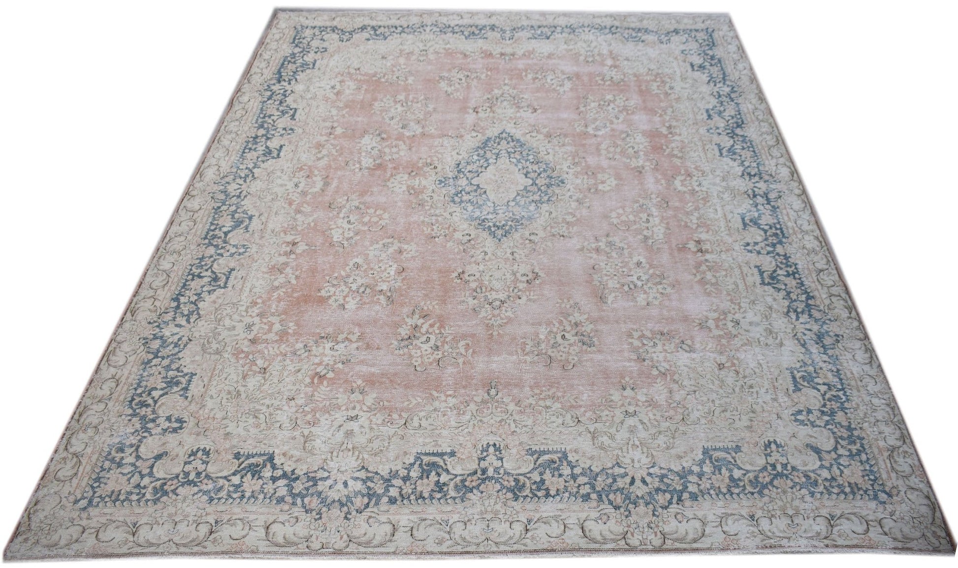 A vintage Persian Kerman rug featuring a central medallion and floral motifs in soft pink and blue.