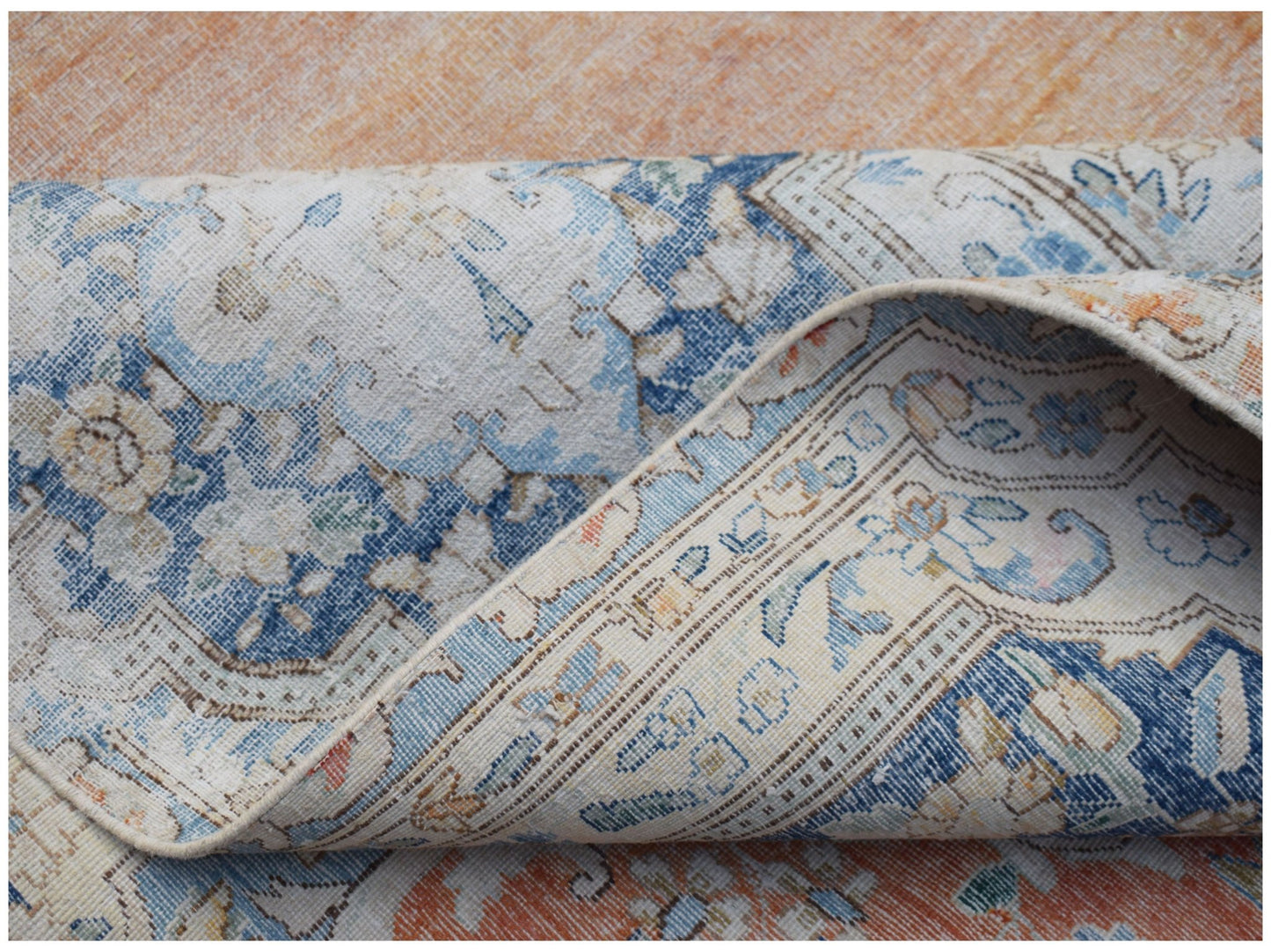A folded vintage Persian Kerman rug featuring intricate blue and orange floral patterns.