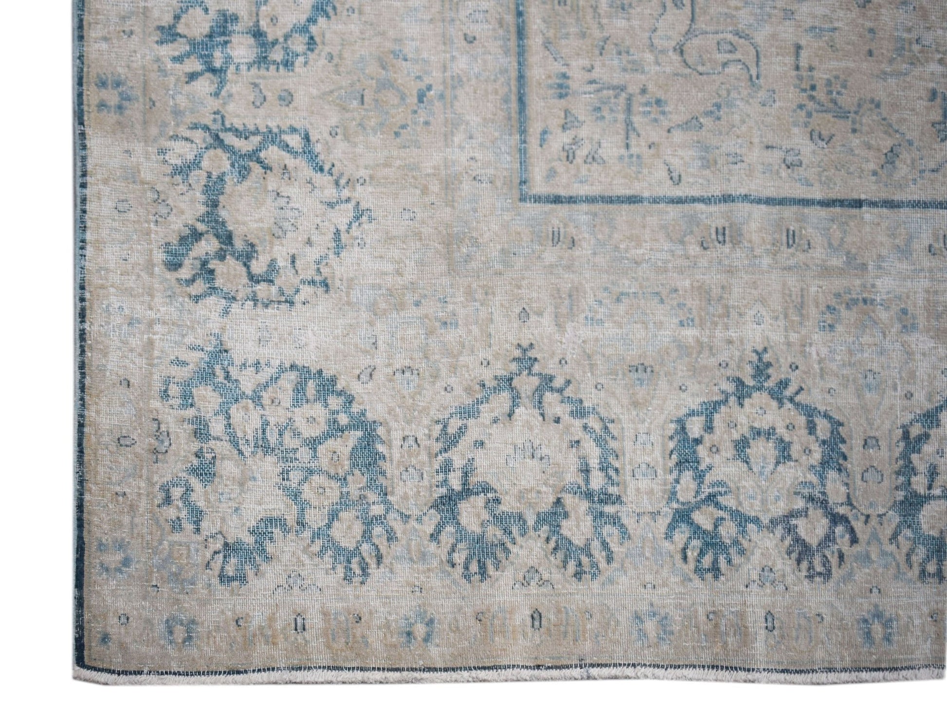 A vintage Persian Kerman rug featuring a faded blue floral pattern on a neutral beige background.