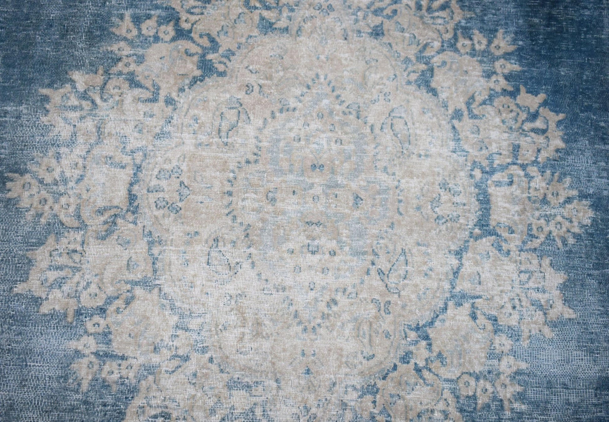 A vintage Persian Kerman rug featuring a central medallion with intricate blue and beige florals.