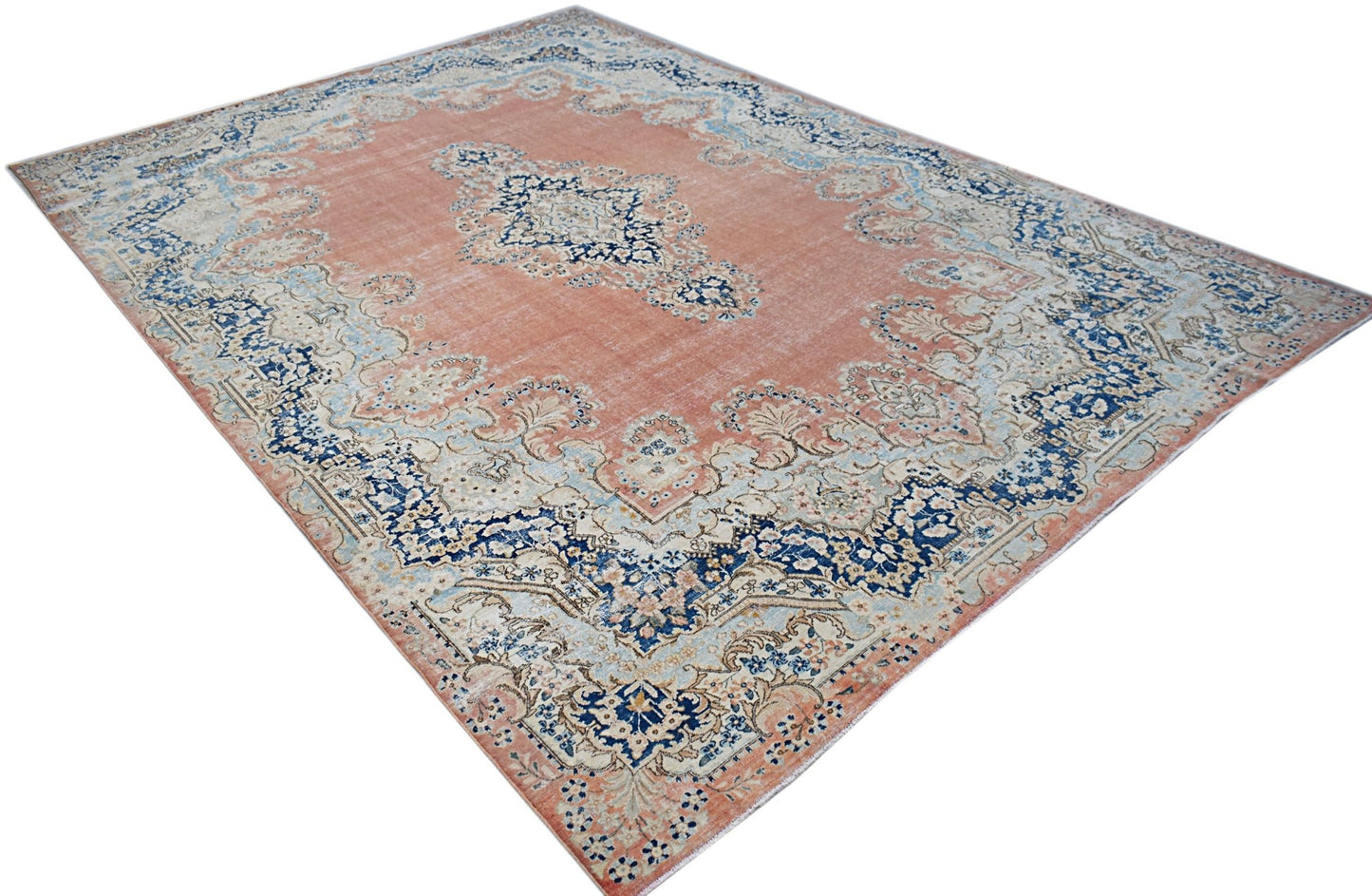 A vintage Persian Kerman rug featuring a central medallion and floral motifs in blue and peach.