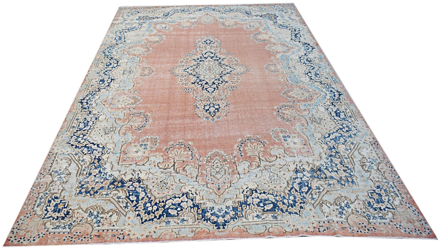 A vintage Persian Kerman rug featuring a central medallion and floral motifs in blue and peach.