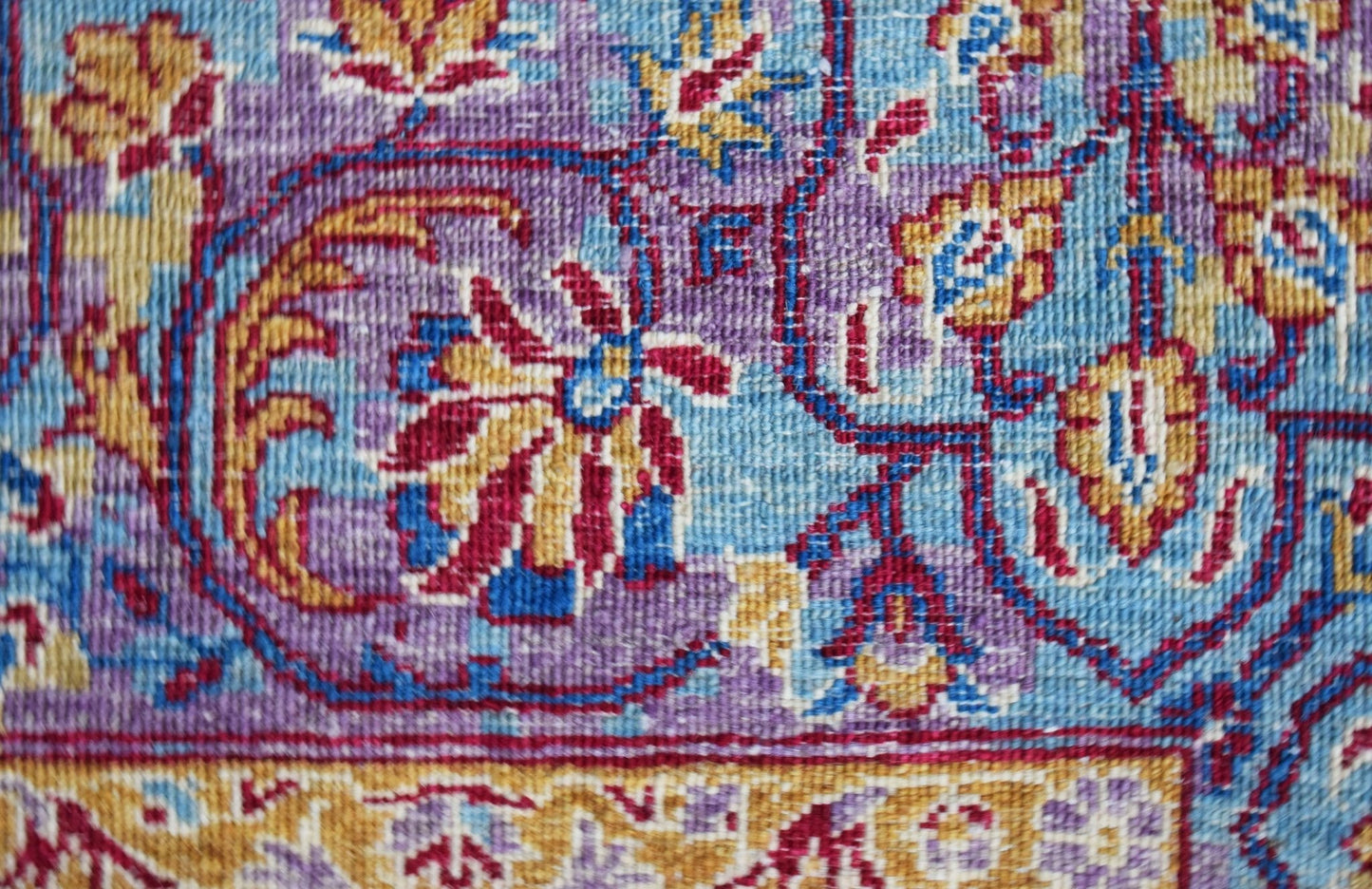 A close-up of a handwoven Afghan Chobi rug featuring intricate floral patterns in blue and purple.