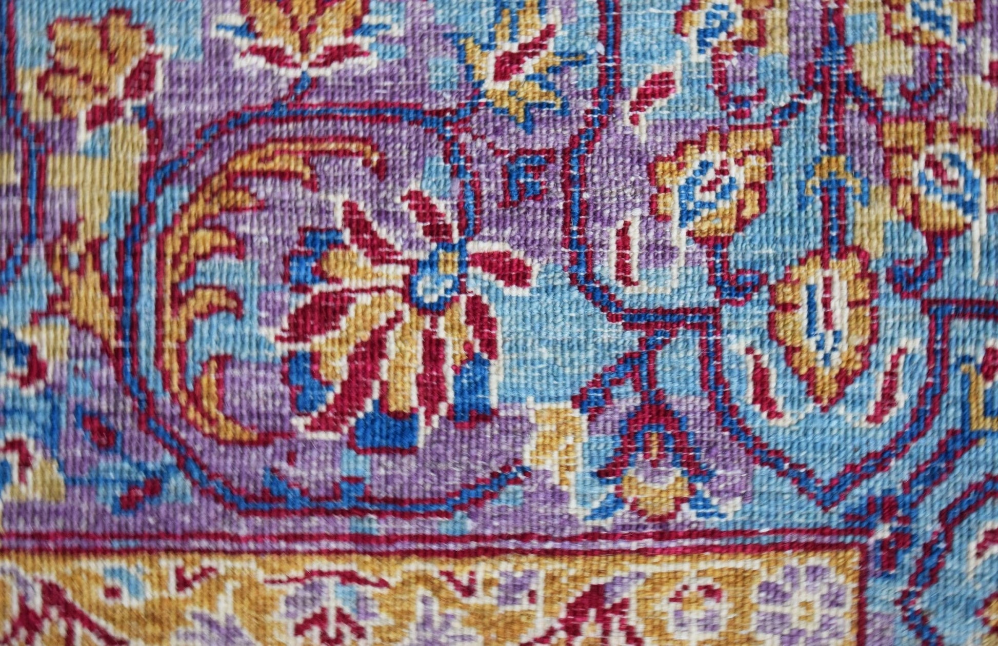 A close-up of a handwoven Afghan Chobi rug featuring intricate floral patterns in blue and purple.