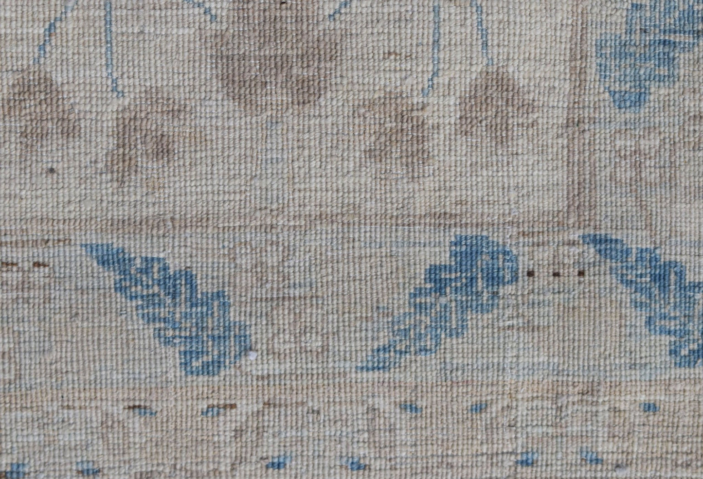 A close-up of a handwoven Afghan Balkh rug featuring blue floral motifs on a beige wool background.